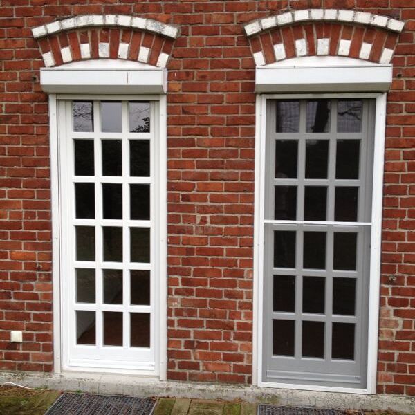 Zwei hohe Sprossenfenster mit weißem Rahmen in roter Ziegelwand