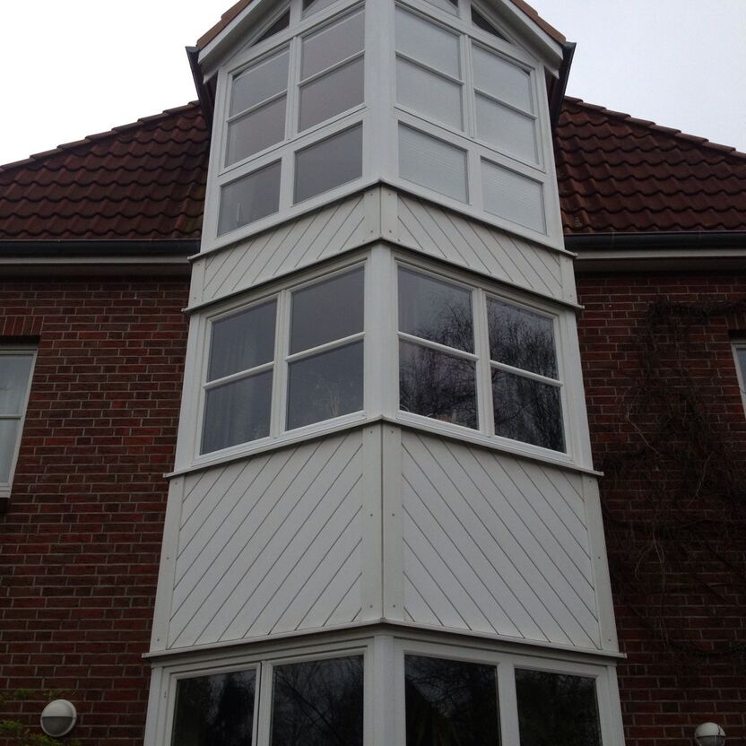 Weißes Hauselement mit Sprossenfenster zwischen roten Ziegelwänden