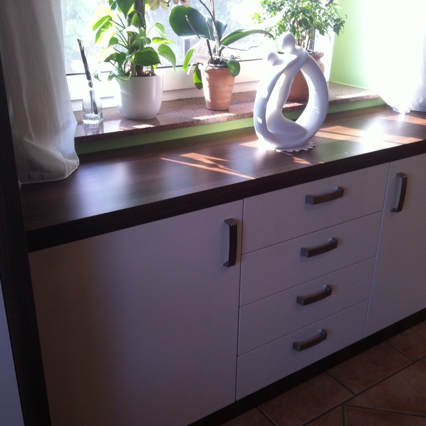 Sideboard aus Holz mit weißen Fronten vor Fensterbank