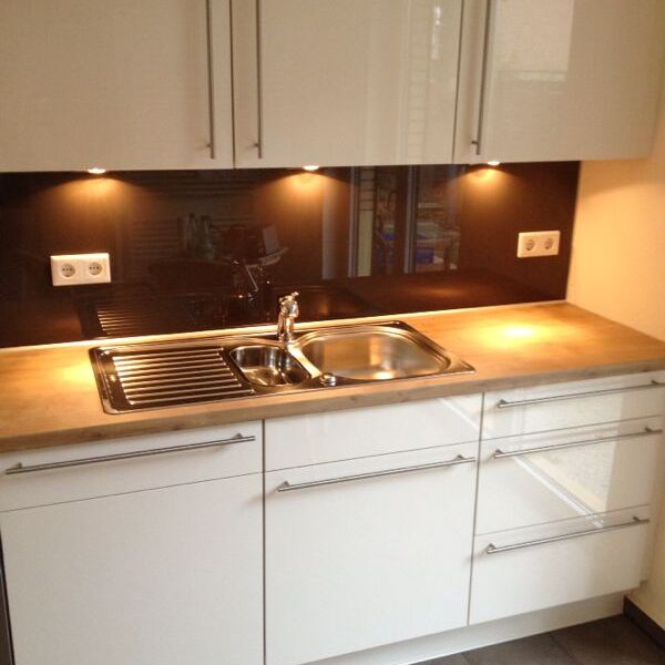 Weiße Küchenzeile mit silbernem Waschbecken unter Beleuchtung