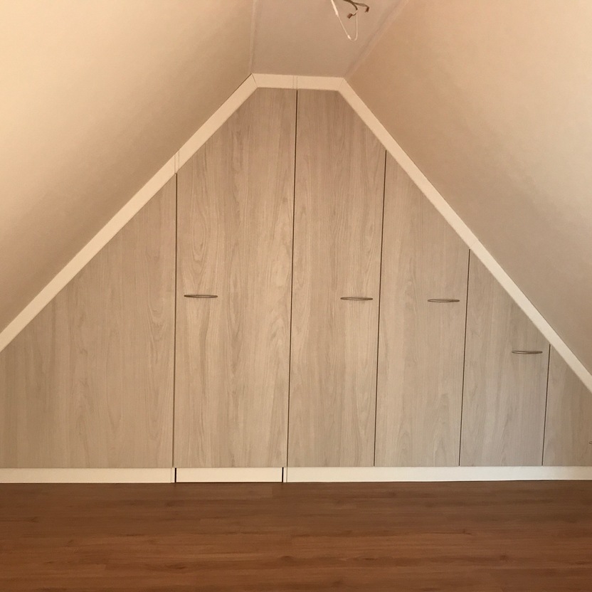 Maßgeschneiderter Innenausbau eines Schrankes mit Holzfronten unter einer spitzen Dachschräge, eingepasst in die Raumgeometrie.