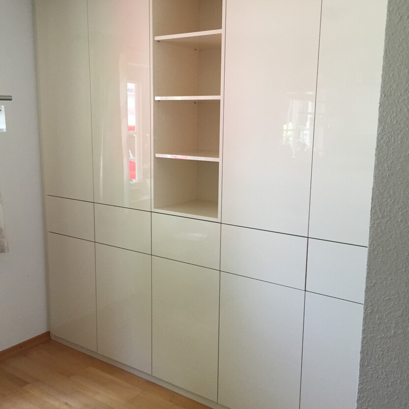 Weißer Schrank als Teil des Innenausbaus mit einer Kombination aus geschlossenen und offenen Regalfächern in einem hellen Raum.