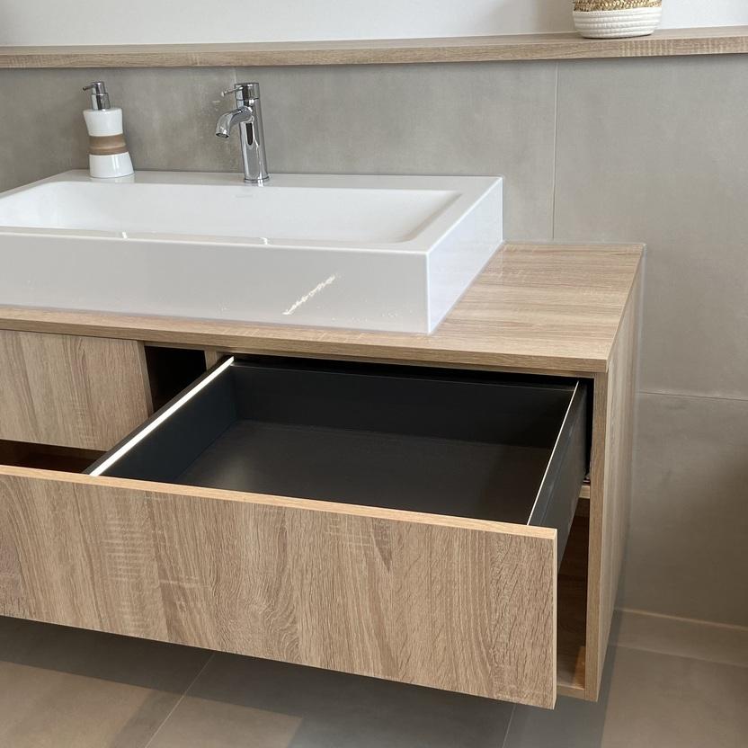 Innovativer Innenausbau in einem Badezimmer mit einem hölzernen Waschtischunterschrank, offenen Fächern und einem aufgesetzten Waschbecken neben einer Toilette.