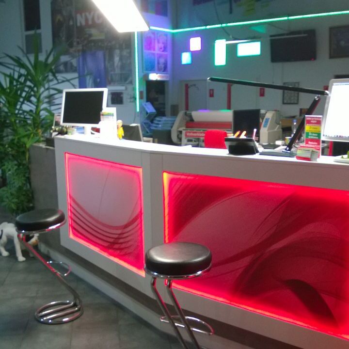 Moderner Innenausbau eines Empfangsbereichs mit leuchtend roter Neonbeleuchtung, Arbeitsstationen, Dekorpflanzen und einem Hund.