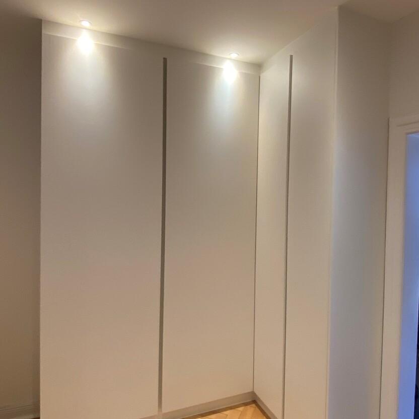 Weißer, maßgefertigter Eckschrank mit integrierter Beleuchtung und Parkettboden in einem modernen Innenausbau.