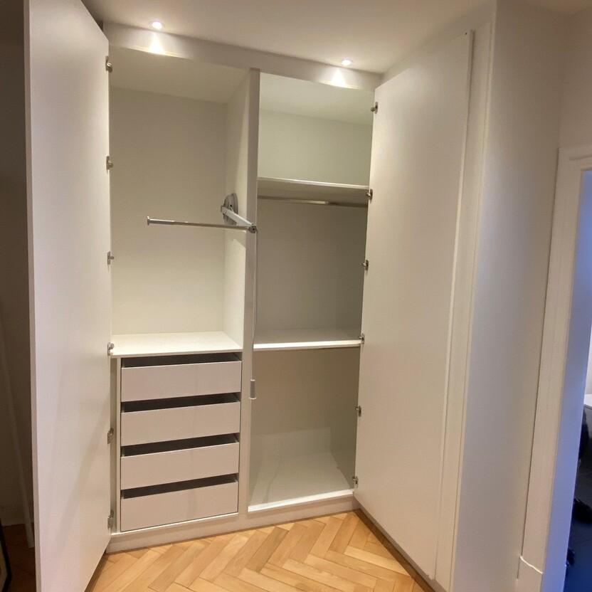 Geöffneter, weißer maßgefertigter Eckschrank mit Schubladen, Regalen und Kleiderstange in einem hochwertigen Innenausbau.