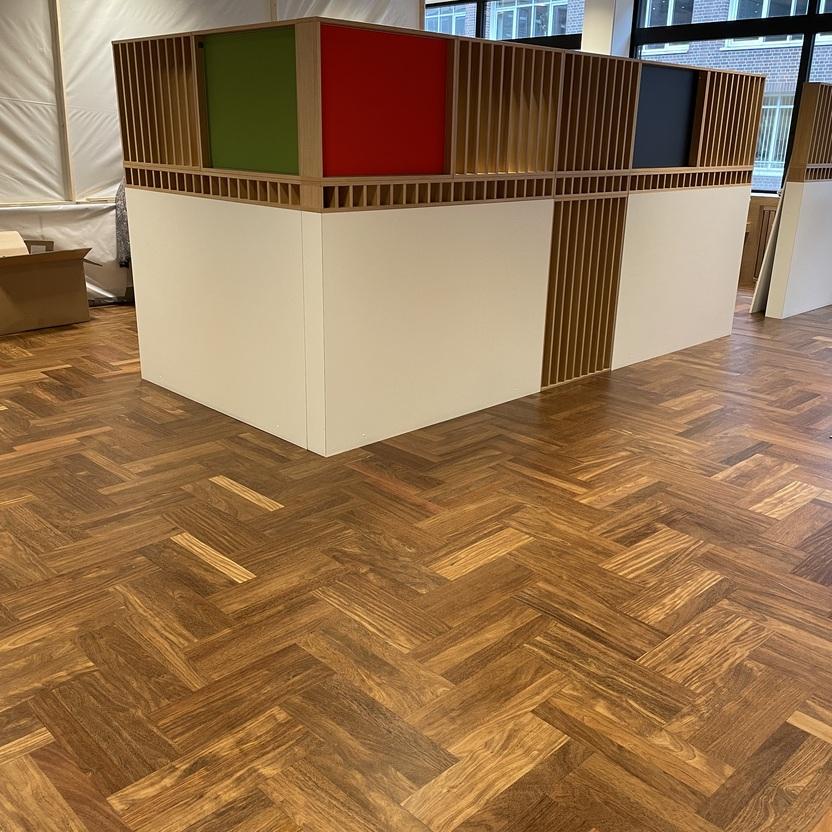 Moderne Trennwand mit grünen, roten und schwarzen Paneelen sowie dekorativen Holzlamellen in einem hochwertigen Innenausbau. Der Raum hat einen eleganten Holzboden in Fischgrätenmuster.