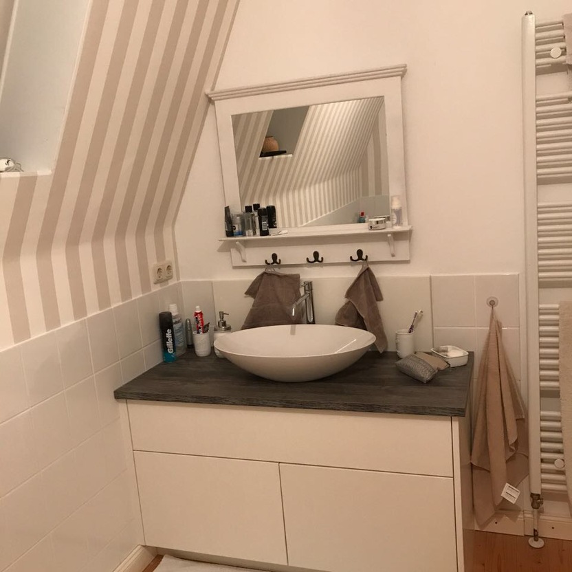 Modernes Badezimmer mit weißem Waschtisch, Aufsatzwaschbecken und Spiegel in einem stilvollen Innenausbau. Das Badezimmer hat schräg gestreifte Wände und einen Handtuchheizkörper.