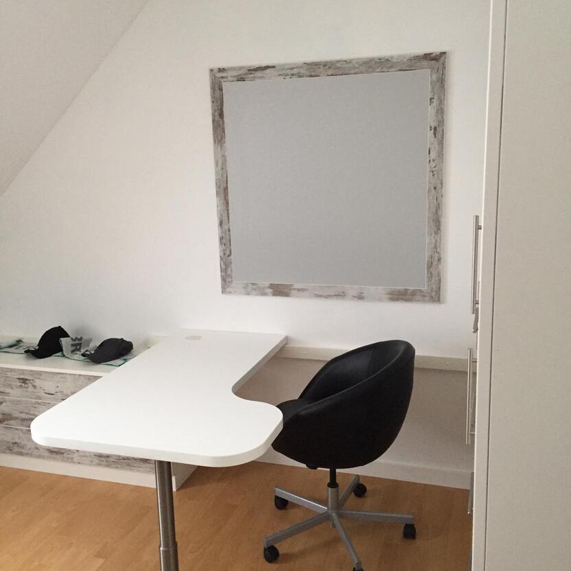 Weiße Schreibtischplatte an Wand montiert vor schwarzem Bürostuhl