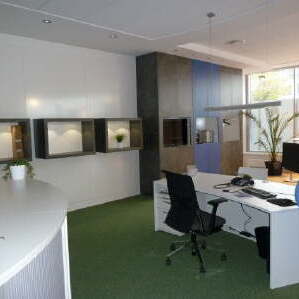 Großraumbüro mit weißem Schreibtisch und schwarzem Schreibtischstuhl auf grünem Boden