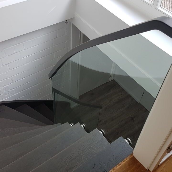 Dunkle Holztreppe mit Glasgeländer und Metallbeschlägen in einem modernen Hausflur mit weißen Wänden.