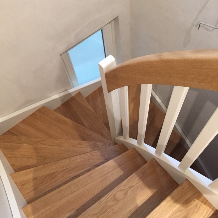 Wendeltreppe aus hellen Eichenholzstufen mit weißen Geländerstäben in einem schmalen Treppenaufgang.