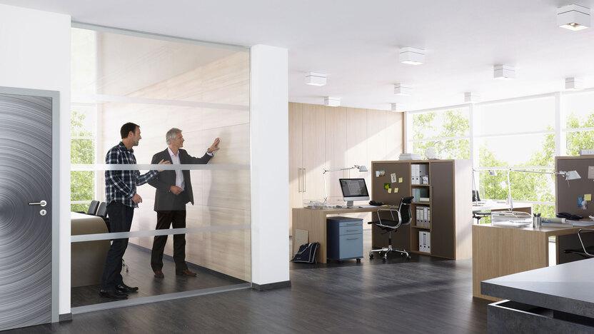 Impression eines Büros mit abgeschlossenem Raum mit Glaswand und offener Bürogestaltung.
