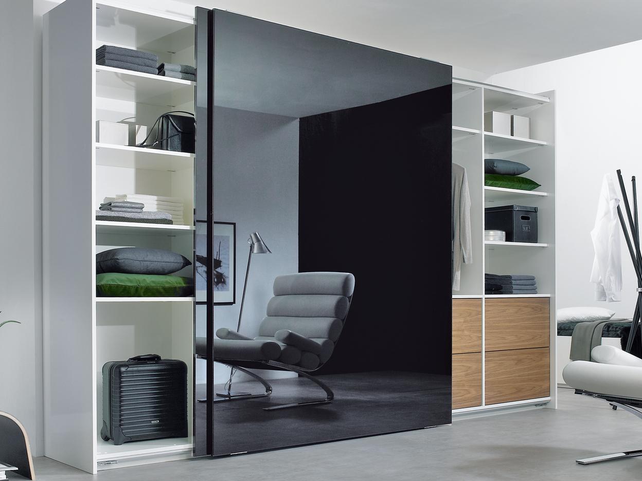 Wohnraumimpression mit abgetrennter dunkler Glasschiebetür für Ruheoase und integrierten Einbauregalen