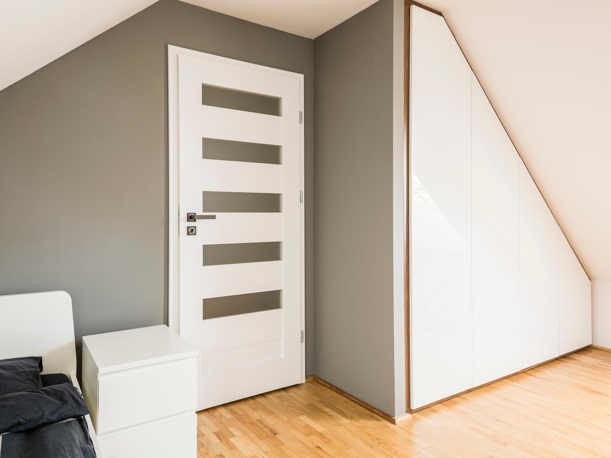 Weißer Einbauschrank an Dachschräge Weißer Einbauschrank an Dachschräge, dreieckig mit Trennwand zur Zimmertür an hellem Parkett.