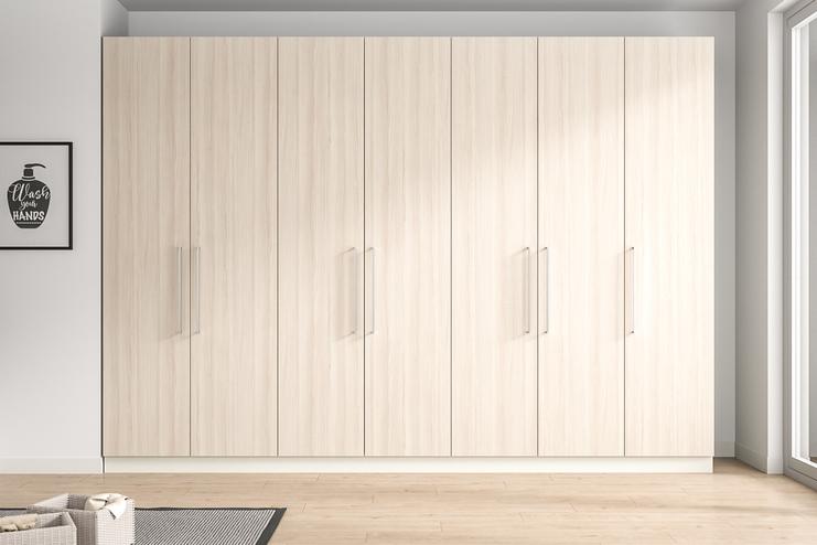 Großer, maßgefertigter Schrank in einem eleganten Zimmer. Wandfüllender, maßgeschneiderter Schrank in heller Holzoptik mit minimalistischen Griffen, der nahtlos in das moderne Raumdesign integriert ist.